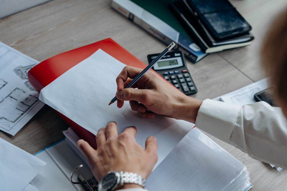 A sleek calculator and a miniature architectural model of a house sit on a professional wooden desk, illustrating the financial planning and cost analysis of selling a property.